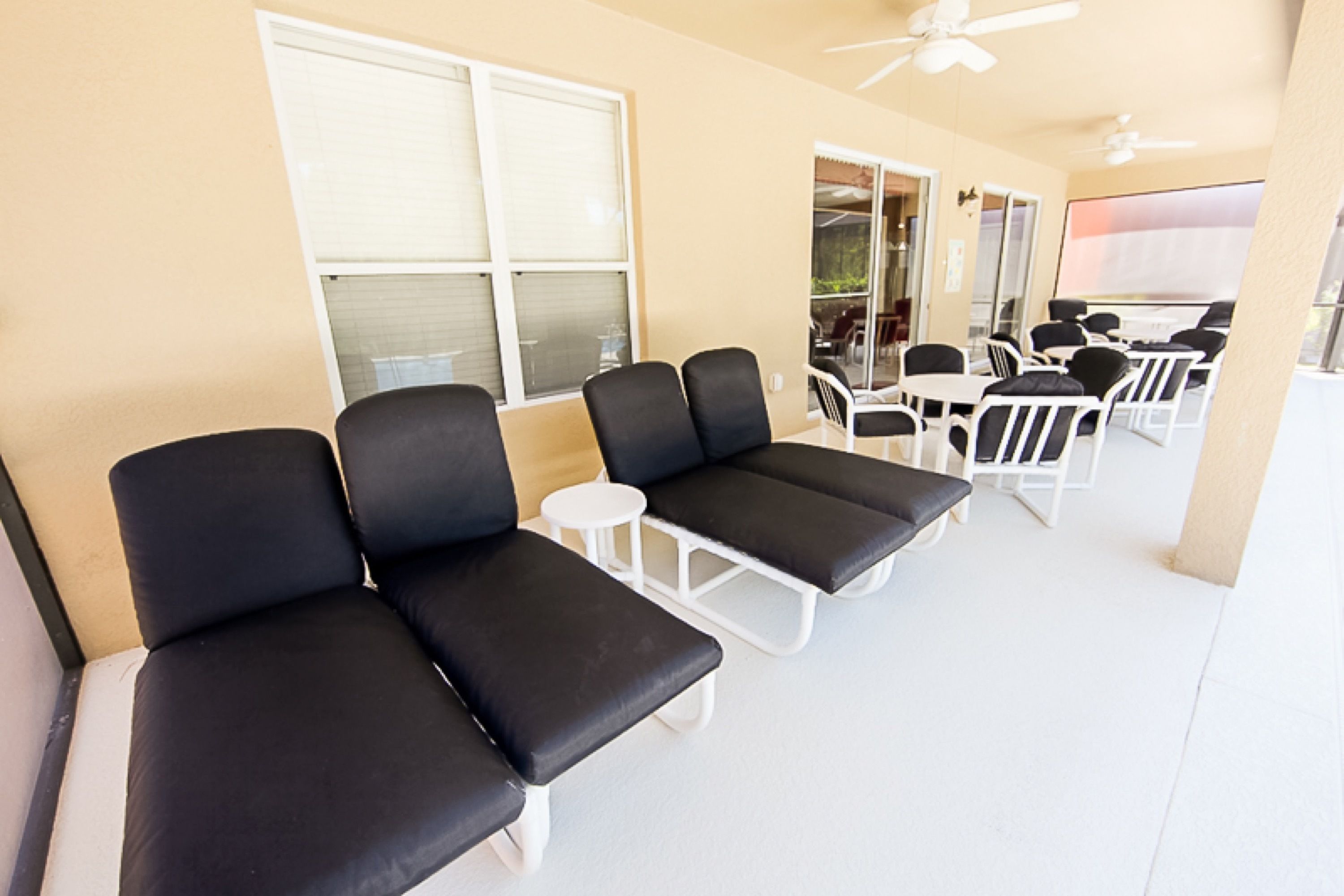 A room with black cushioned seating, white tables, and ceiling fans.