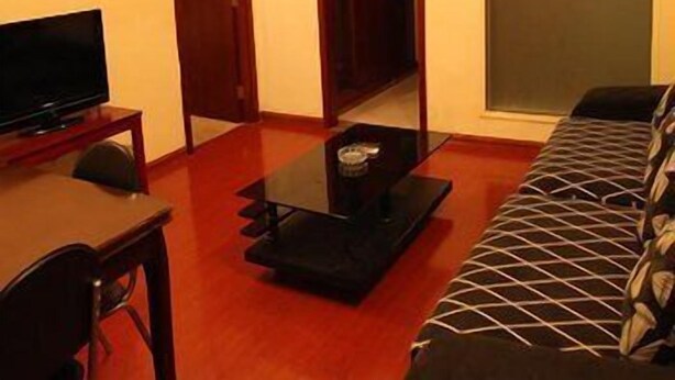 A living room with a sofa, a TV on a stand, and a glass coffee table. - Greentree Inn Wuxi Guangrui Road Hotel (Wuxi)