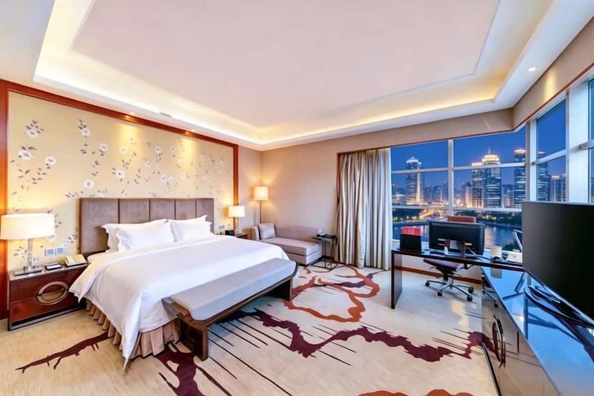 Ein Hotelzimmer mit Bett, Schreibtisch, Fernseher und Blick auf die Stadt.