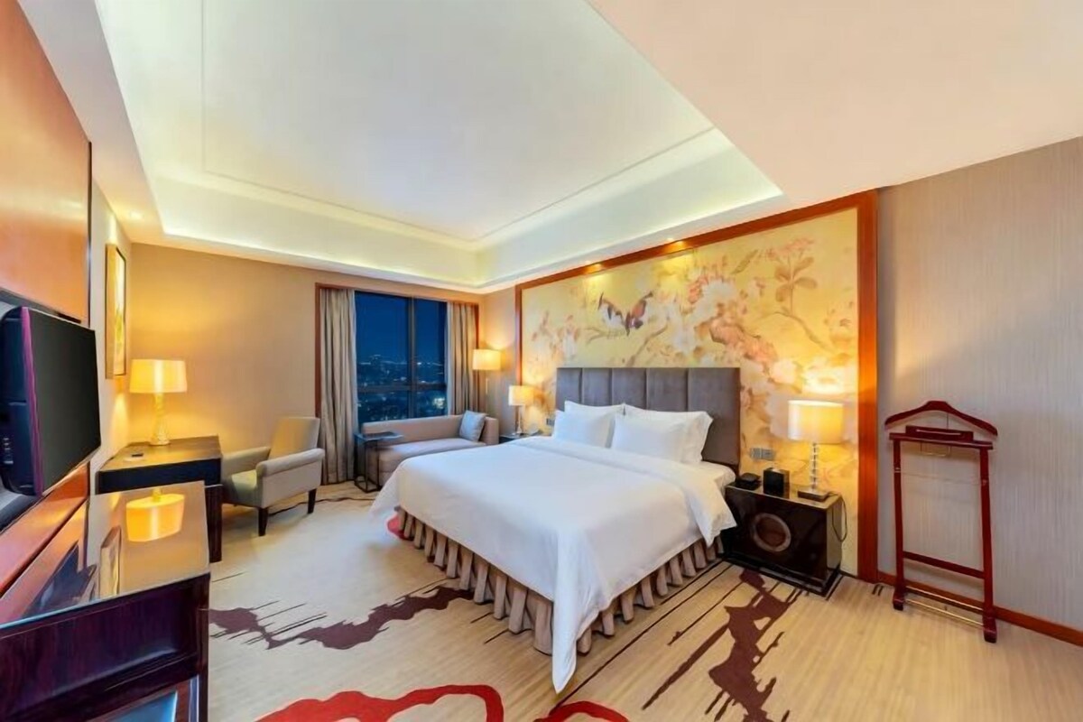 Habitación de hotel con una cama grande, televisión, escritorio y vistas a la ciudad.