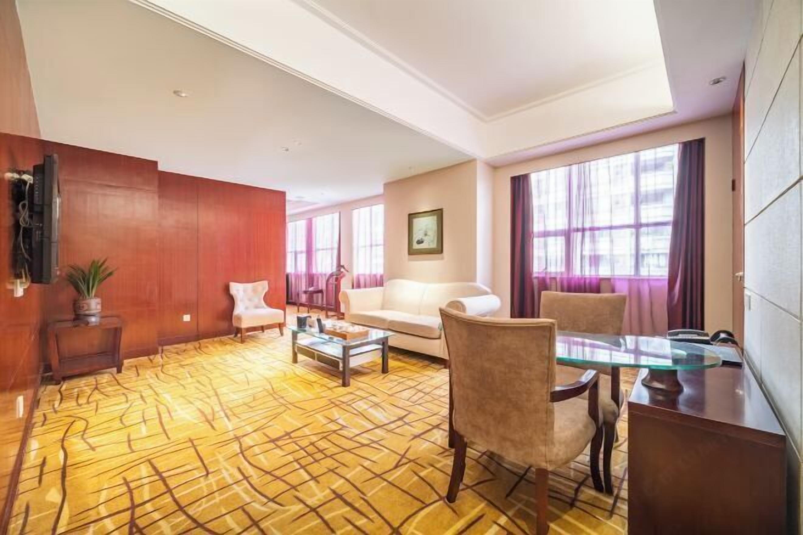 Ein Hotelzimmer mit einem gemusterten Teppich, einem Sofa, einem Sessel, einem Couchtisch und einem Fernseher.