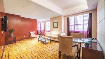 Ein Hotelzimmer mit einem gemusterten Teppich, einem Sofa, einem Sessel, einem Couchtisch und einem Fernseher.