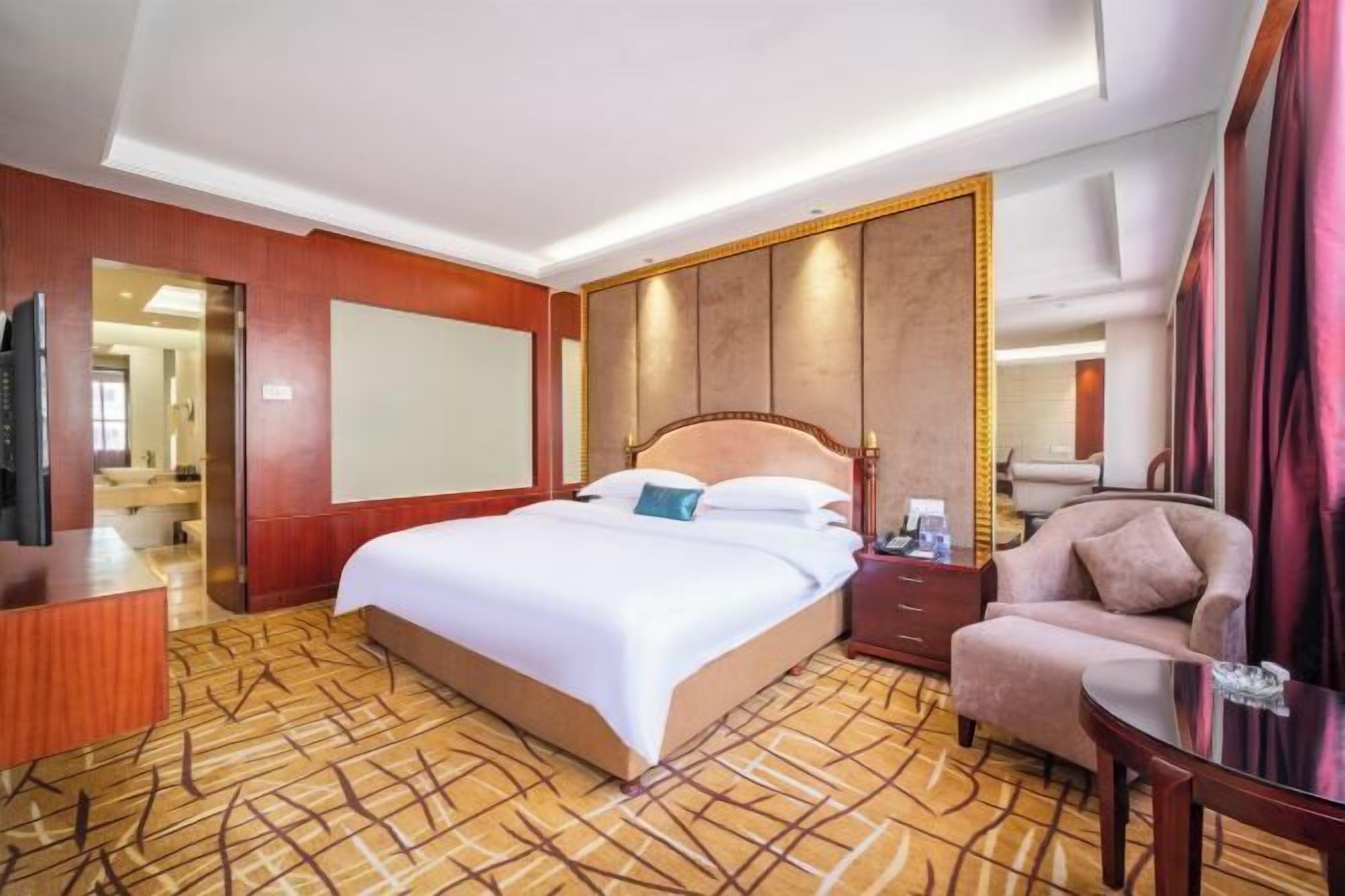 A hotel room with a large bed, a wooden nightstand, a desk, and a chair.