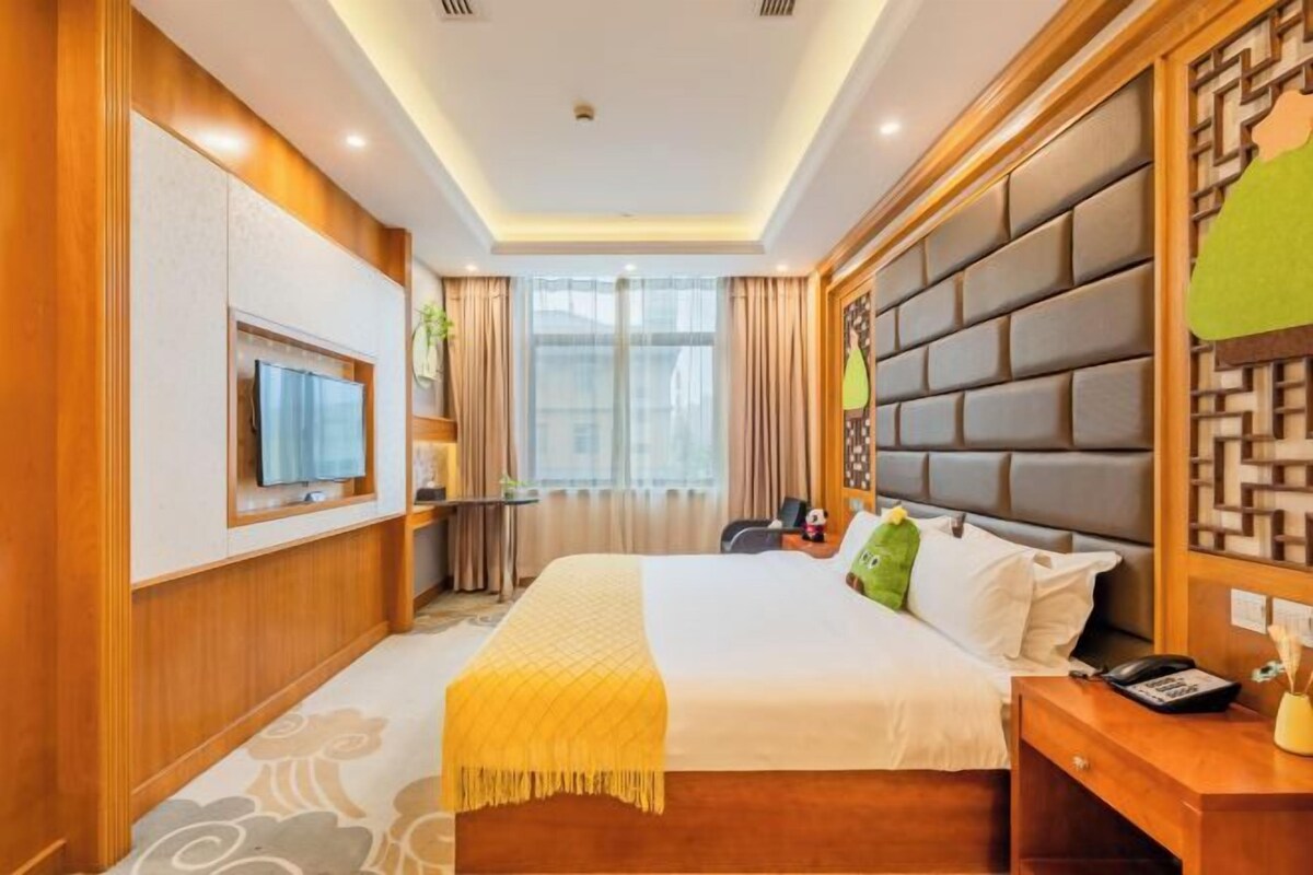 A hotel room with a bed, a TV, a desk, and a window with curtains.