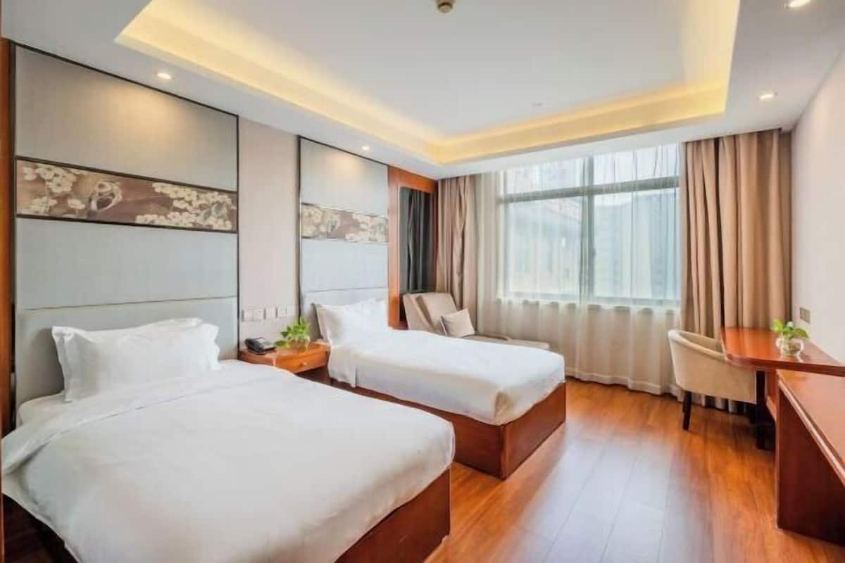 Een hotelkamer met twee bedden, een bureau, een stoel en een groot raam met gordijnen.