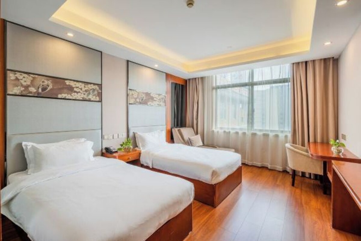 A hotel room with two beds, a desk, a chair, and a large window with curtains.