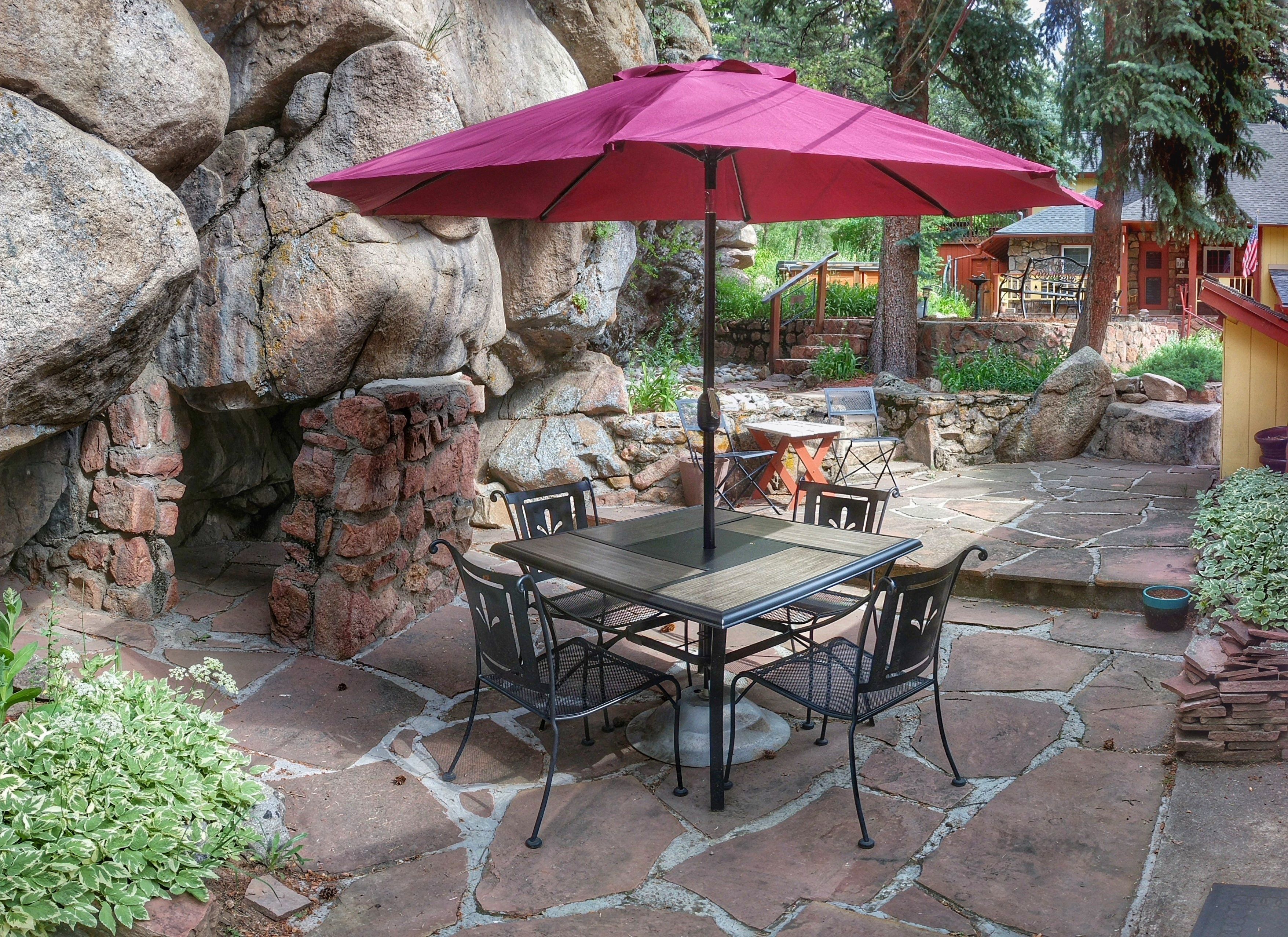 A patio with a table and chairs, a red umbrella, and a stone wall.
