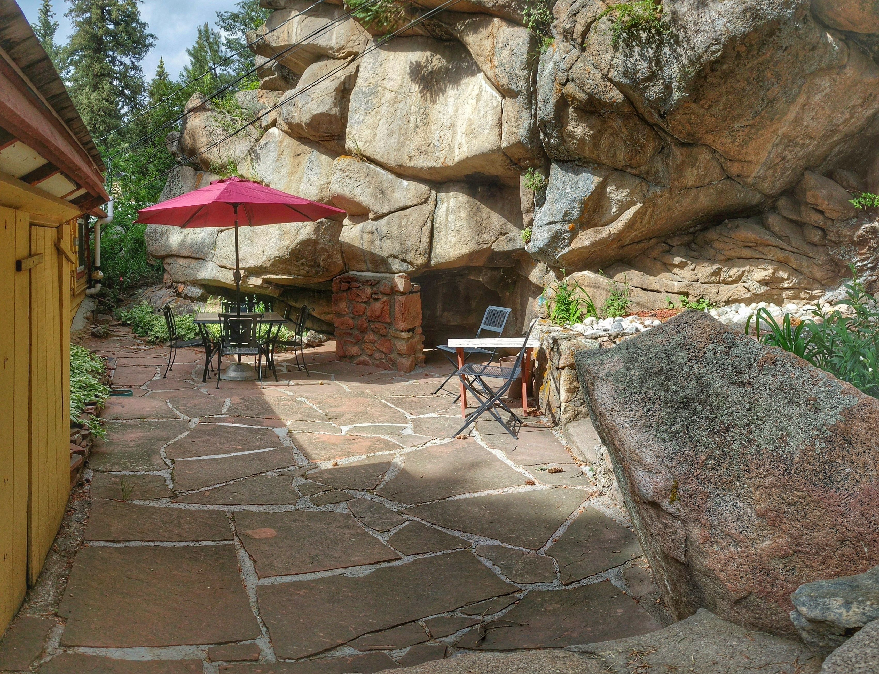 A stone patio with a table and chairs, a red umbrella, and a stone wall.