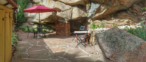 A stone patio with a table and chairs, a red umbrella, and a stone wall.