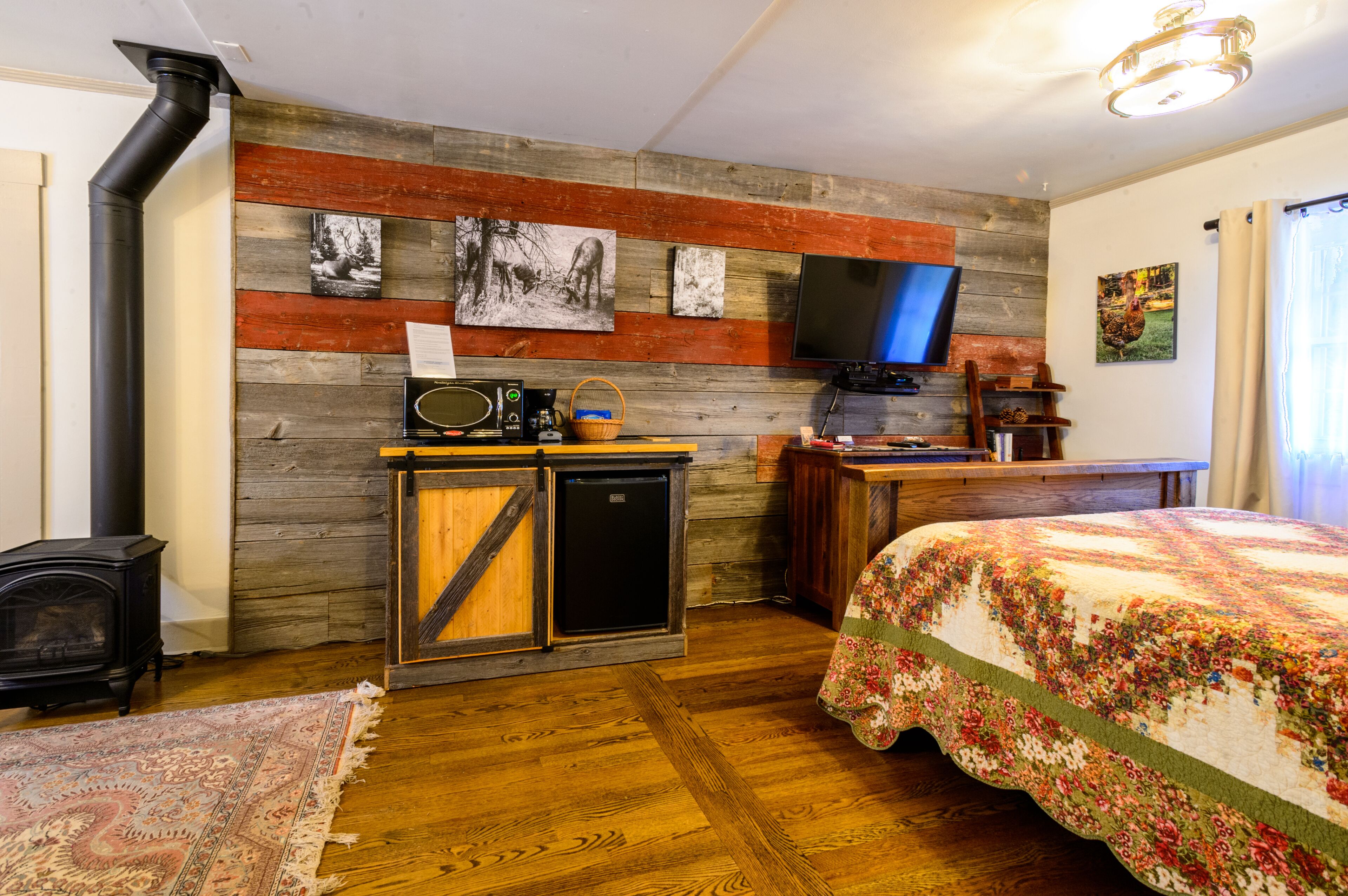 Una habitación acogedora con una pared de madera, una cama con colcha estampada, una pequeña kitchenette y un televisor.