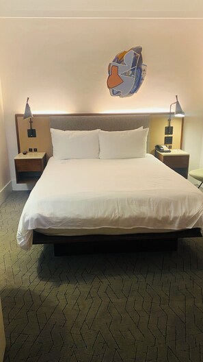 Ein Hotelzimmer mit einem großen Bett, zwei Nachttischen mit Lampen, einem Wandbild und einem Teppichboden.