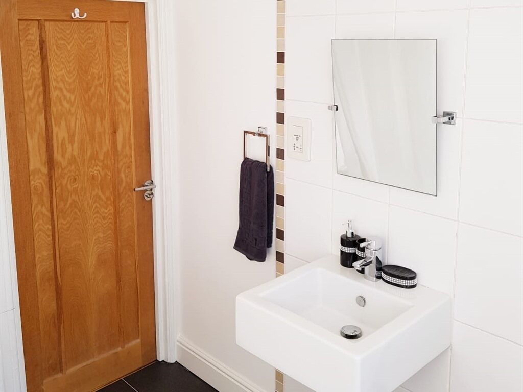 Ein Badezimmer mit Holztür, Waschbecken mit Spiegel darüber und einem Handtuch an einem Halter.