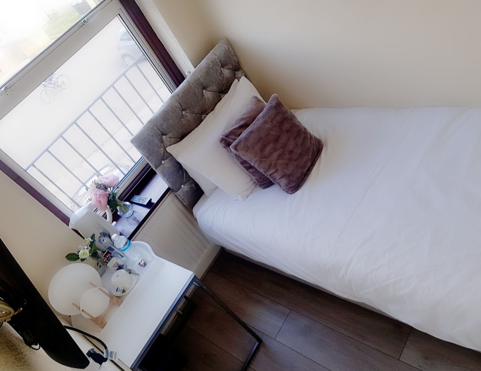A neatly made bed with a headboard, a bedside table with a lamp, and a window with a view of the outside.