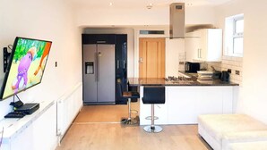 A modern kitchen with a built-in fridge, a TV mounted on the wall, and a small bar area with stools. - The 329 (Enfield)