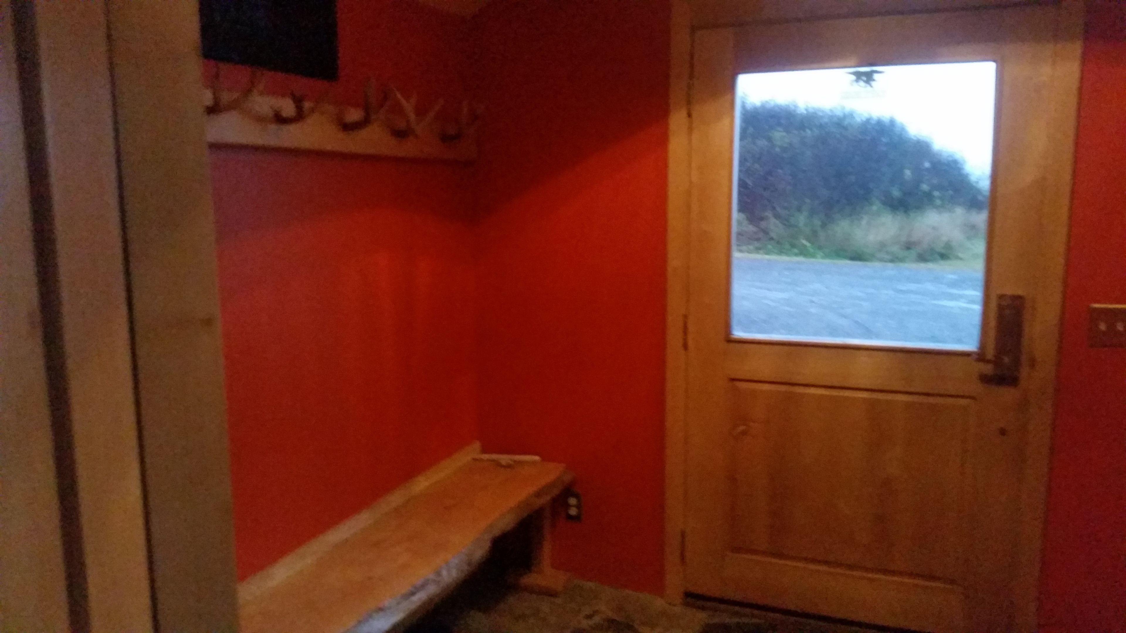 A red-walled hallway with a wooden bench, a door with a window, and a small shelf with items.