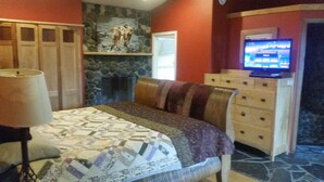Un dormitorio con cama, cómoda, televisor y pared de piedra.