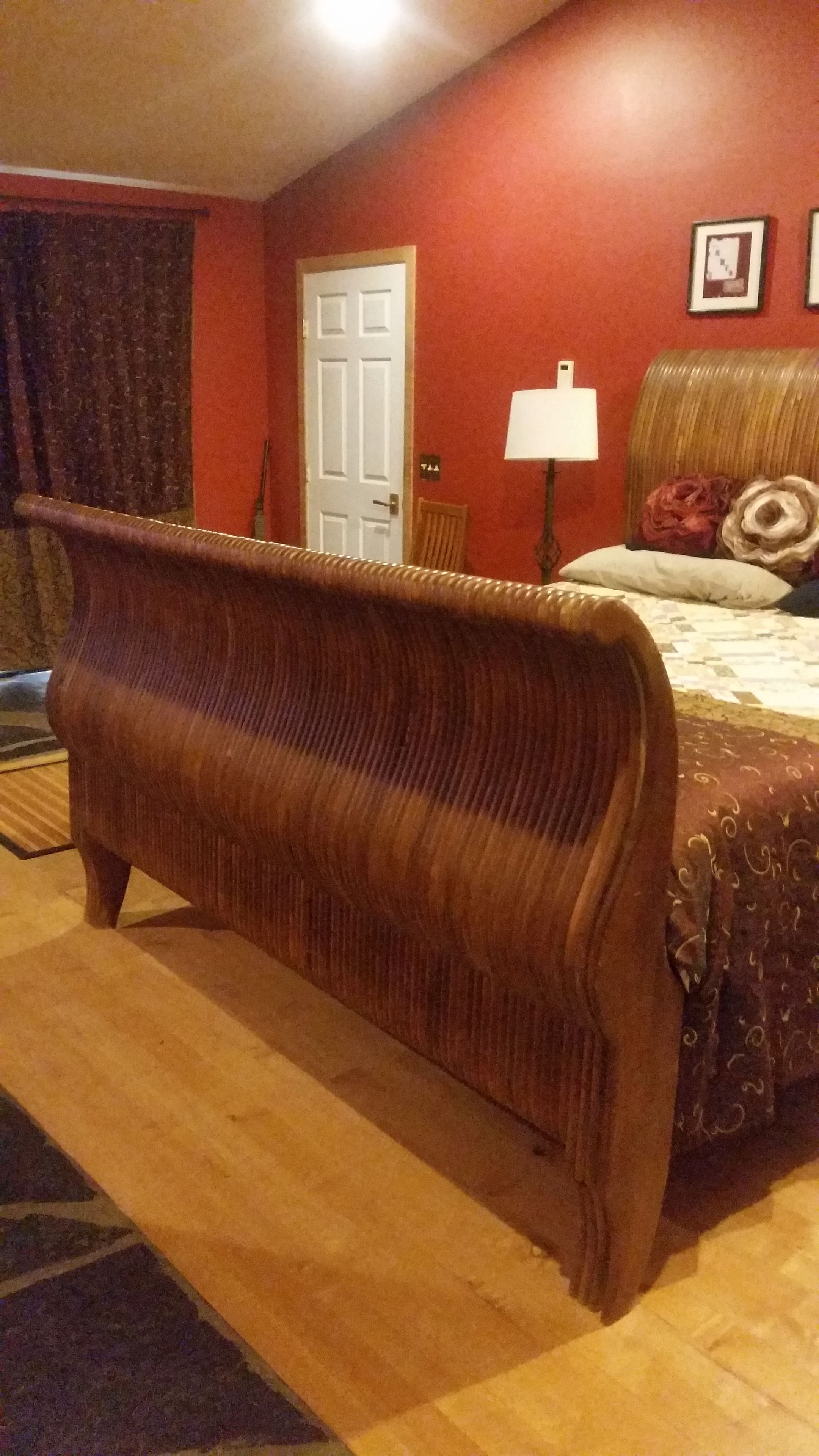 A room with a wooden bench, a bed with a patterned bedspread, a lamp, and a door.