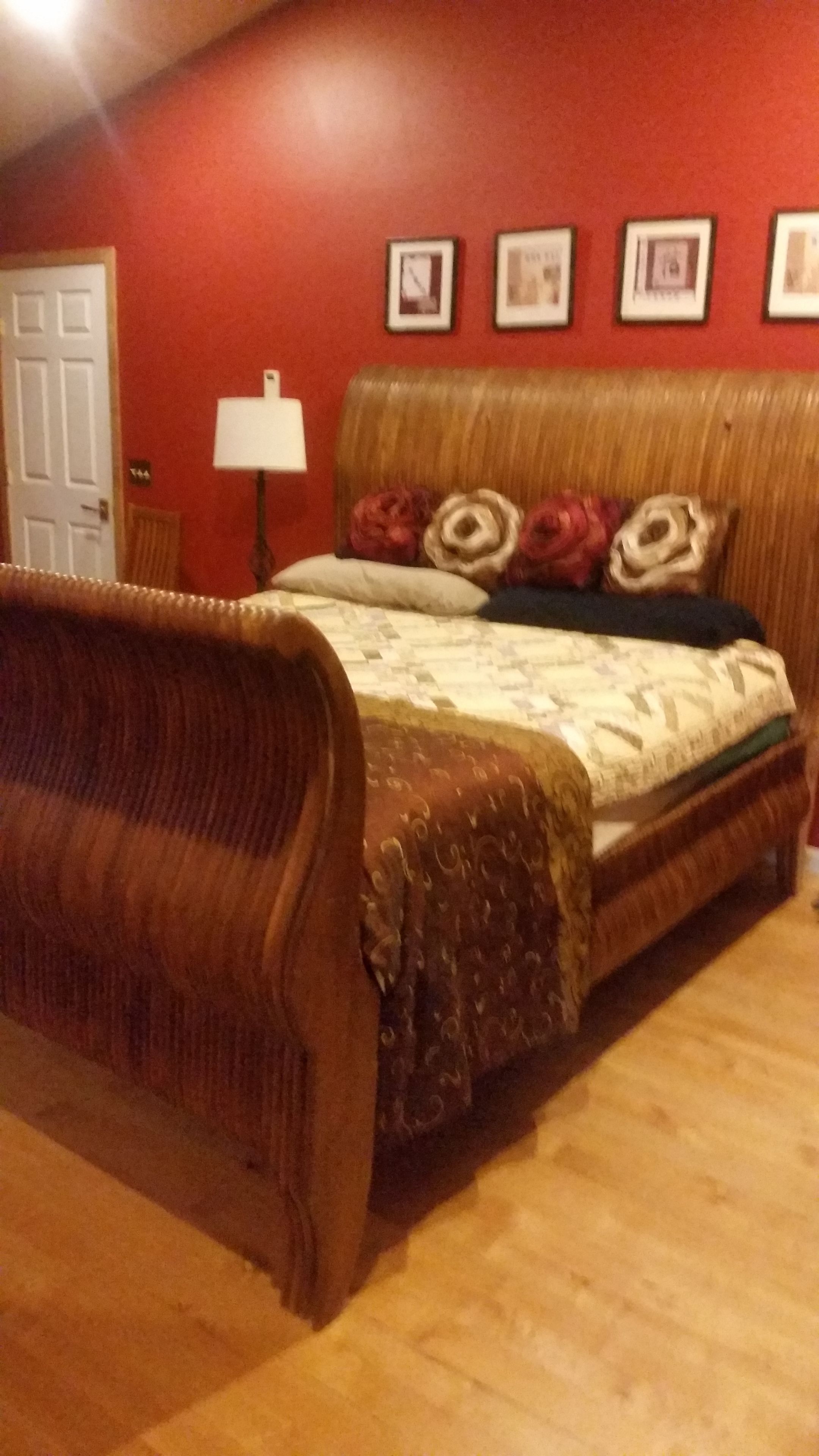 Quarto com cabeceira de madeira, cama com roupa de cama floral e parede vermelha com quadros.