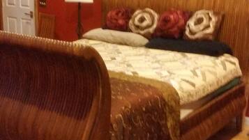 Quarto com cabeceira de madeira, cama com roupa de cama floral e parede vermelha com quadros.