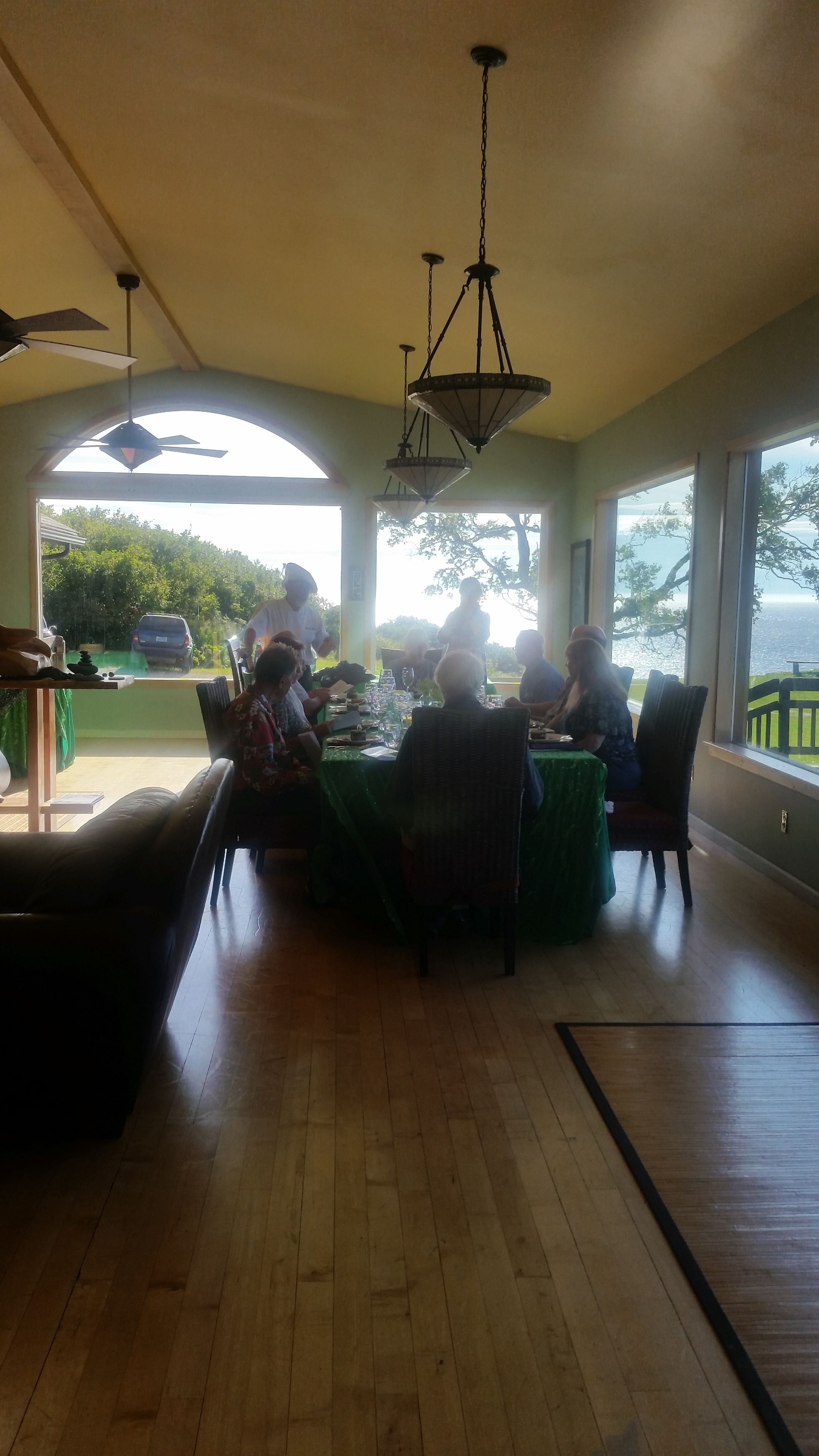 A dining area with a high ceiling, large windows, and a view of the outdoors.