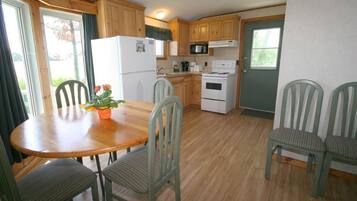 A compact kitchen with wooden cabinets, a refrigerator, a microwave, and a stove. There is a dining table with chairs and a potted plant on it.