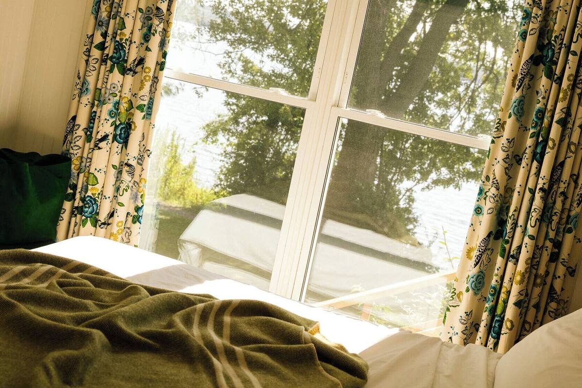 Un dormitorio con cama, ventana con cortinas y vista a árboles fuera.