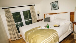 Ein ordentlich gemachtes Bett mit einer gestreiften Decke, ein Nachttisch mit Lampe und ein Fenster mit Vorhängen.