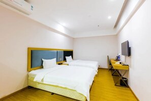 A hotel room with two beds, a desk, a television, and an air conditioning unit.