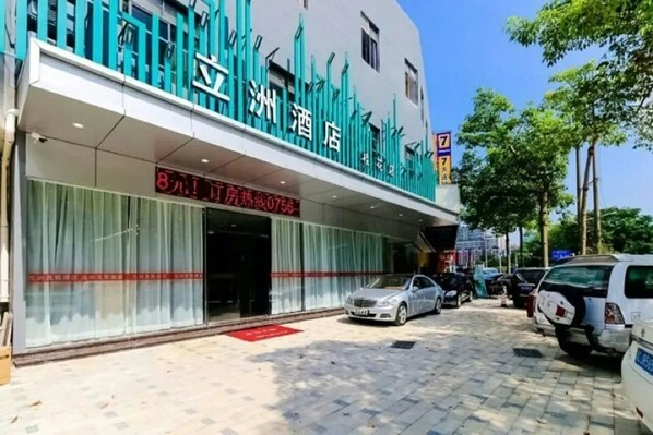 A hotel with a modern facade, a visible entrance, and a parking area with several cars.