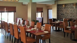 A spacious dining area with multiple tables and chairs, a chandelier, and a stone wall. - Bhutan Boutique Residency (Thimphu)