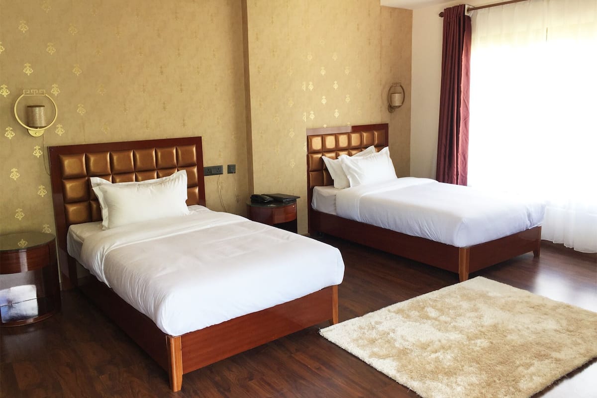 A hotel room with two beds, wooden headboards, a fluffy rug, and a wall with a floral pattern.