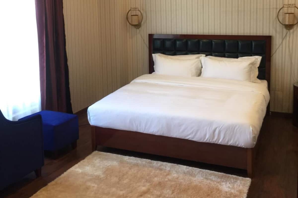 A neatly made bed with white linens, a wooden headboard, and a beige rug on a wooden floor.