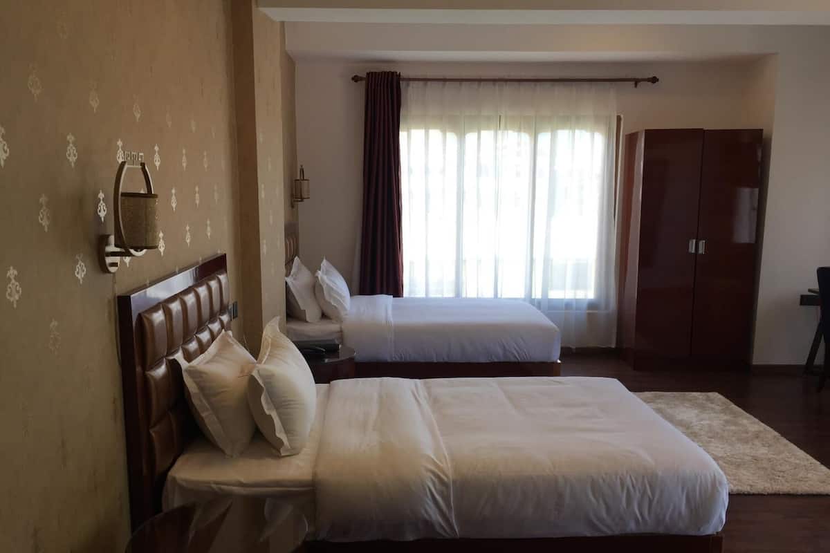 A hotel room with two beds, a wooden wardrobe, a bedside table, and a large window with curtains.