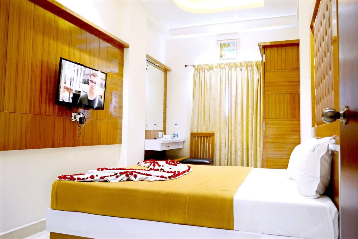 Una habitación de hotel con cama, televisor montado en la pared, baño con espejo y puerta de madera.