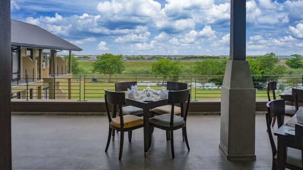 An outdoor dining area with a table set for four, overlooking a scenic landscape with a body of water and trees. - Amora Lagoon (Seeduwa - Katunayake)