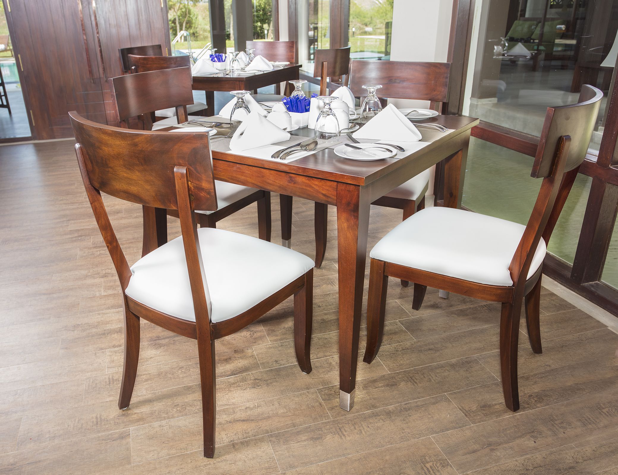 A dining area with a wooden table set for four, surrounded by chairs with white cushions.