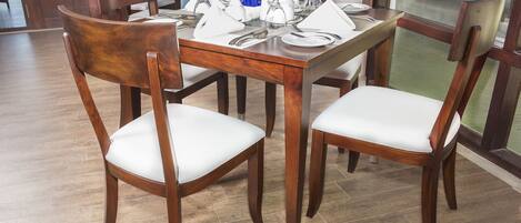 A dining area with a wooden table set for four, surrounded by chairs with white cushions.