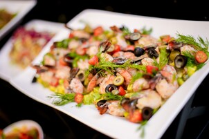 Una bandeja de mariscos con camarones, aceitunas y vegetales sobre un plato blanco.