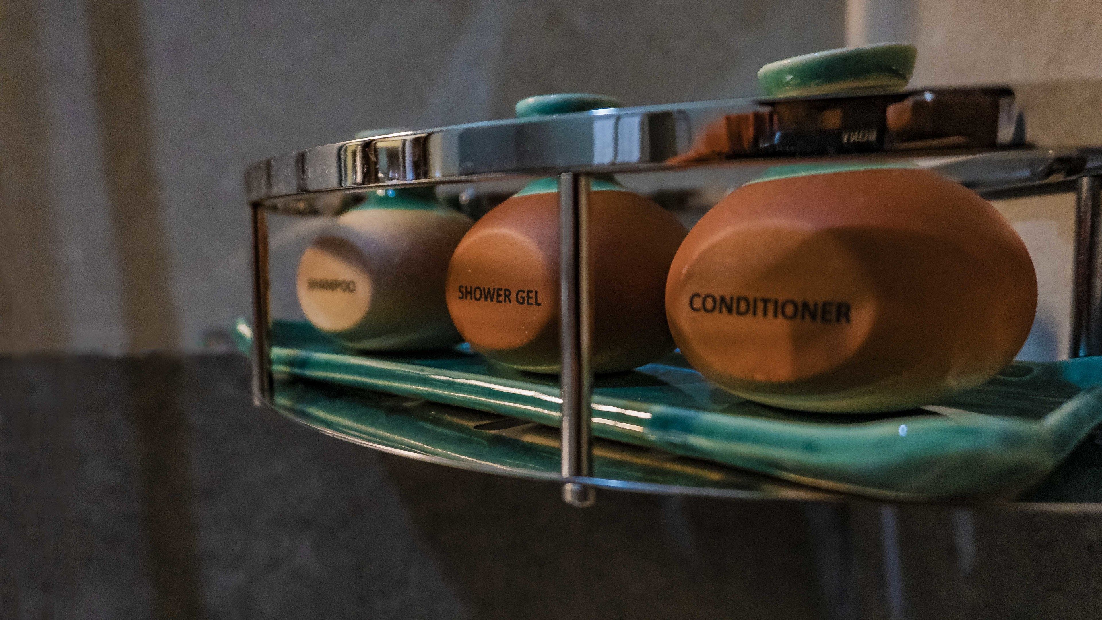 Une étagère de salle de bain contenant trois produits de toilette : du shampoing, du gel douche et un après-shampoing.