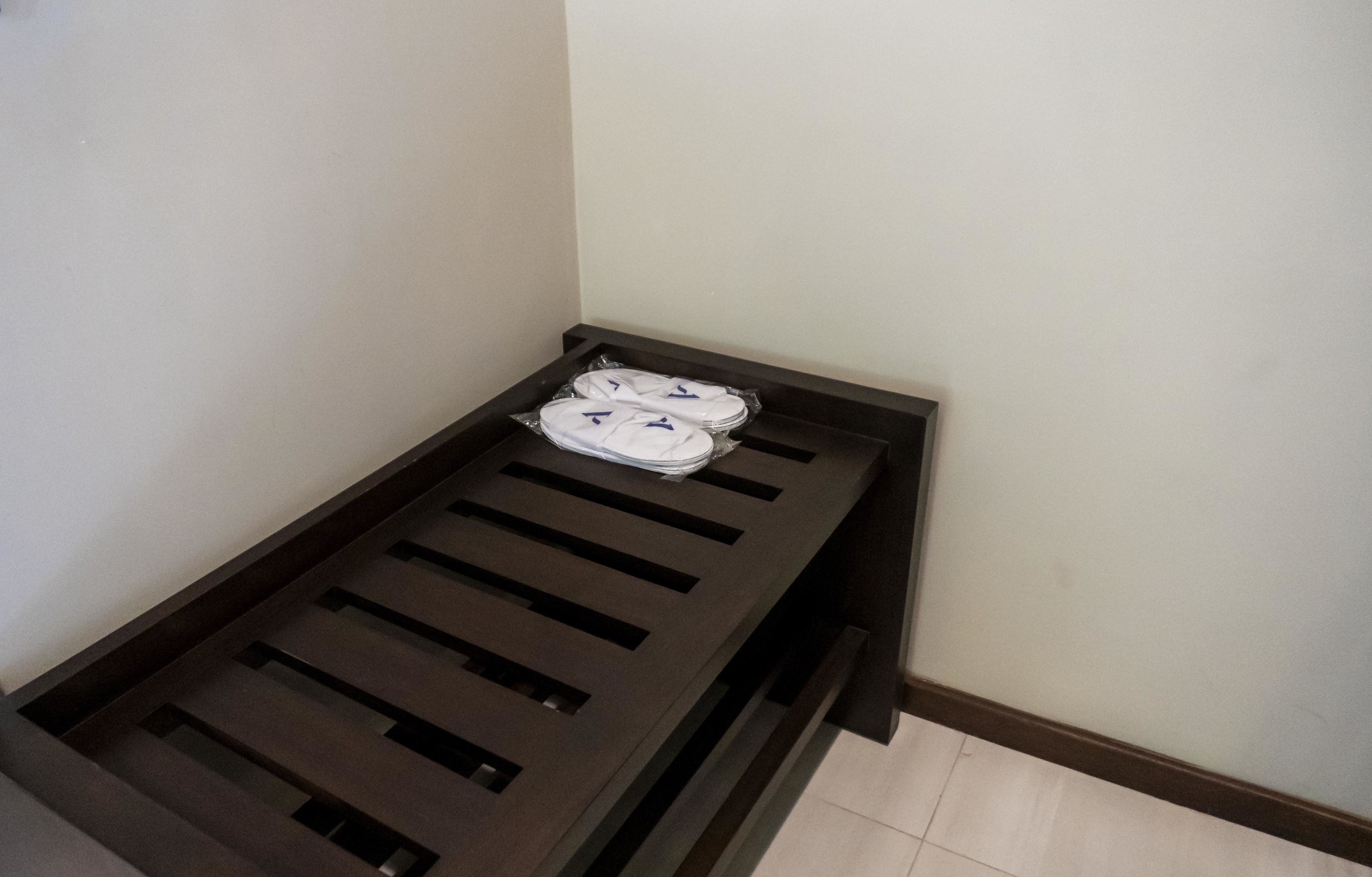 A small, dark-colored metal bed frame with a mattress and pillows in a corner of a room.