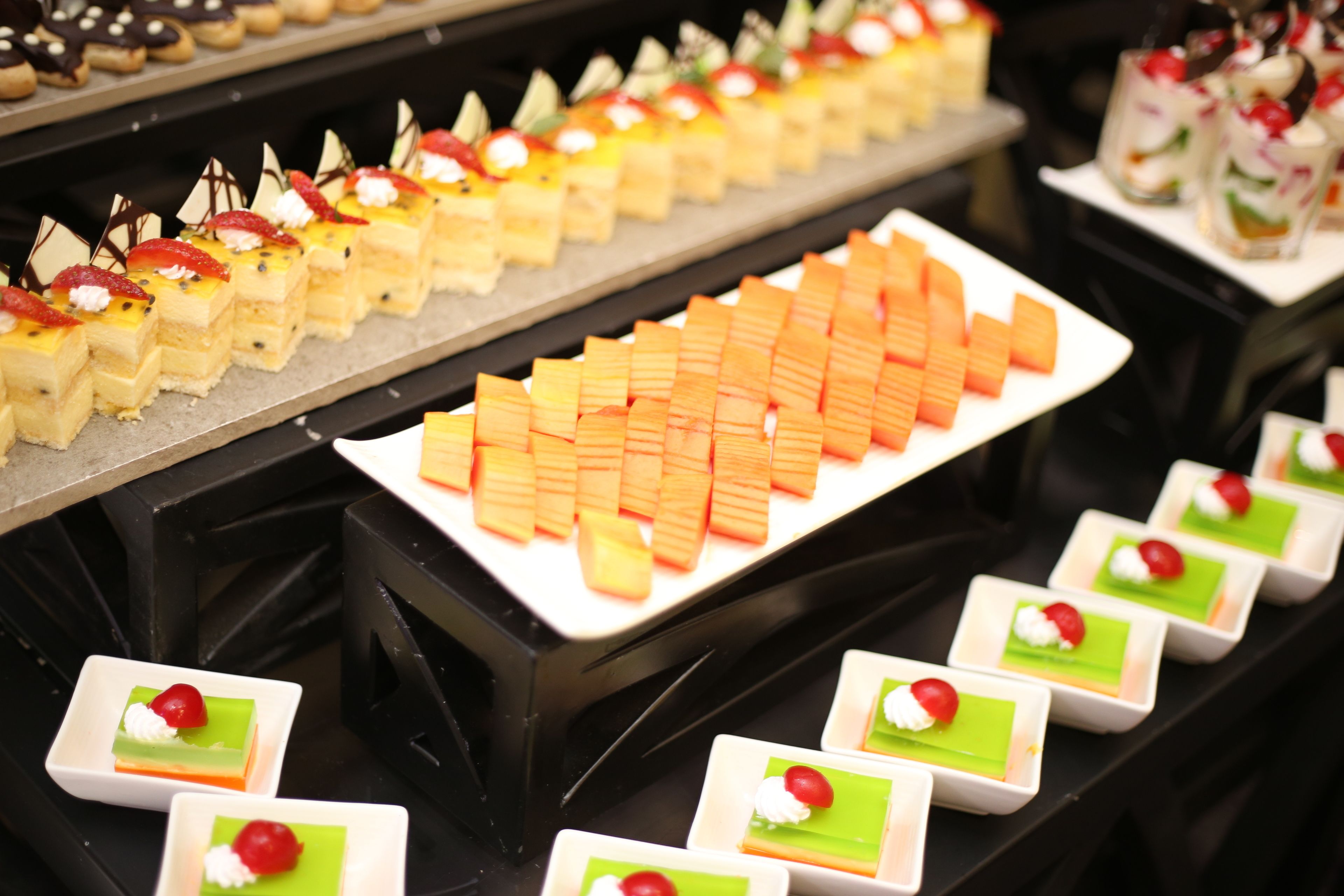 A dessert display with various square-shaped desserts arranged on trays.