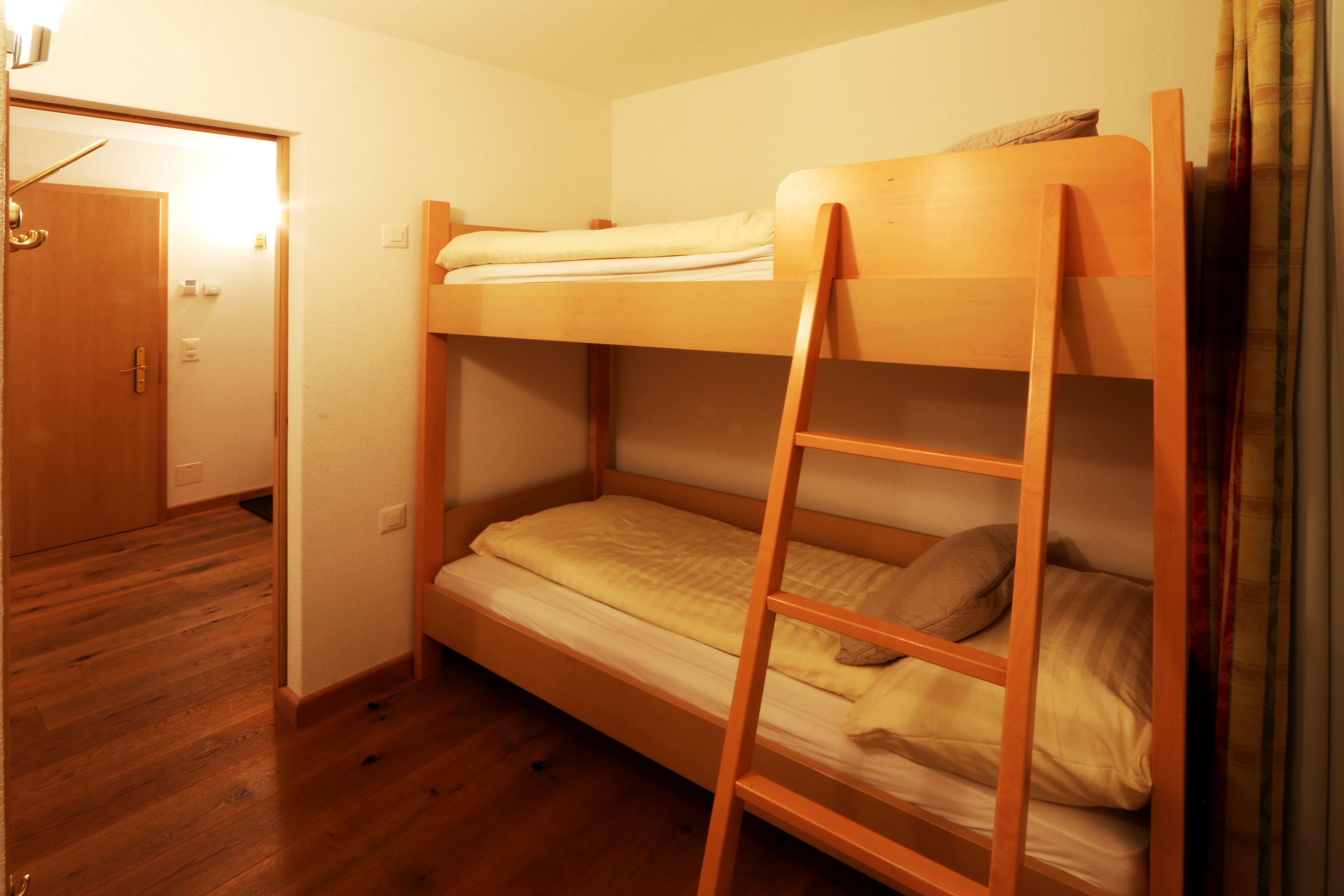 A bunk bed room with a wooden ladder, a door, and a wooden floor.
