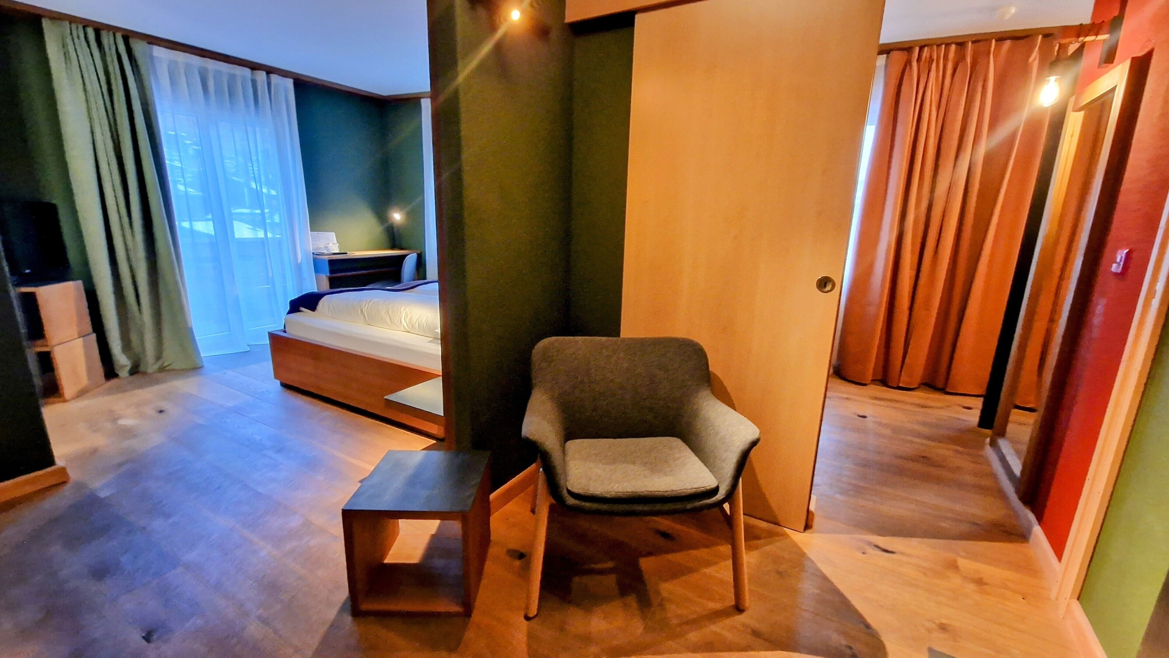 A hotel room with a bed, a chair, a small table, and a wardrobe.