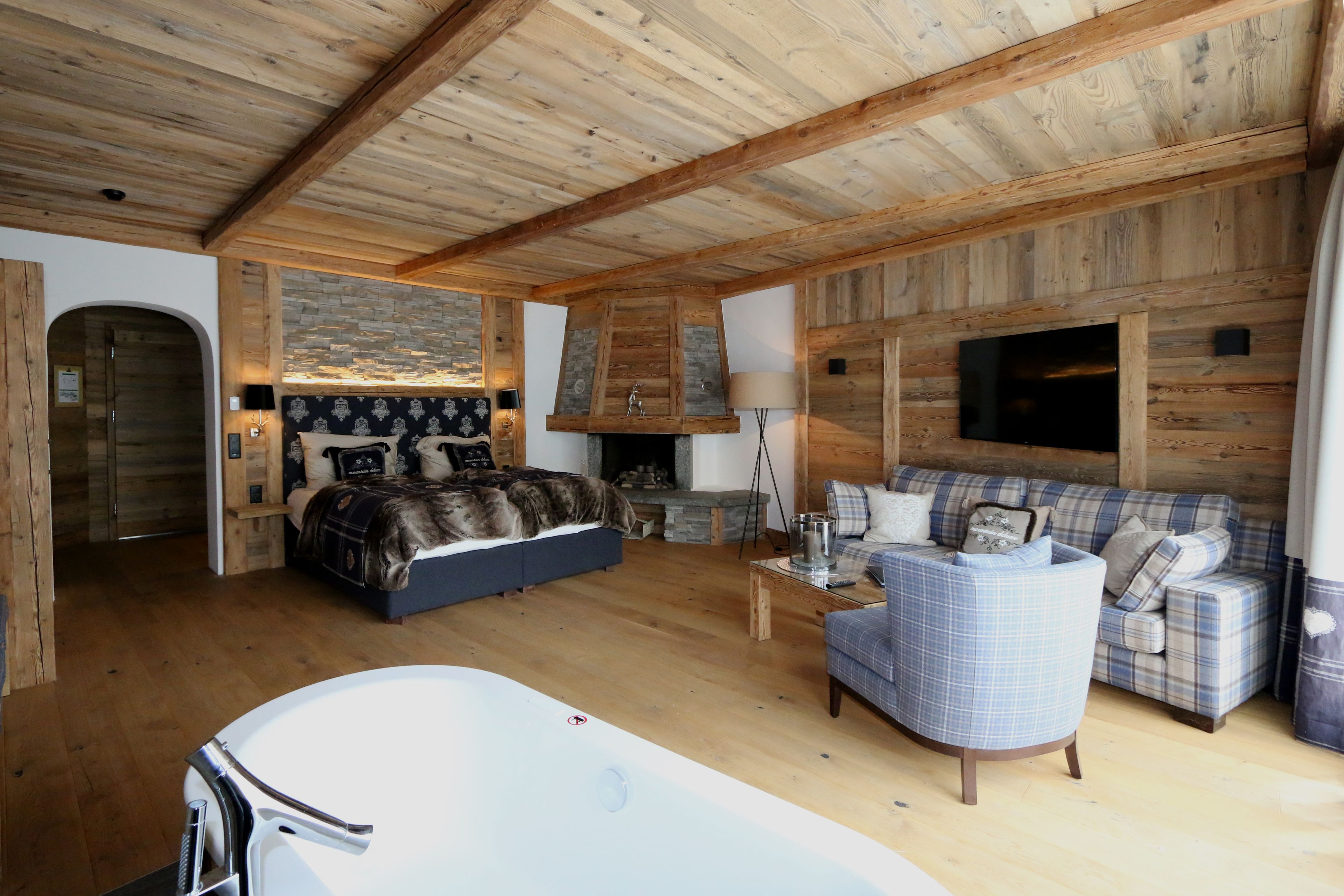 Una habitación acogedora con techo de madera, chimenea, sofá, cama y bañera.
