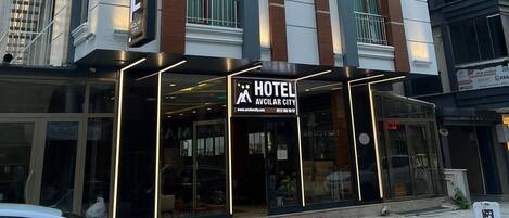 A modern hotel building with a prominent 'HOTEL' sign, large windows, and a red carpet entrance.