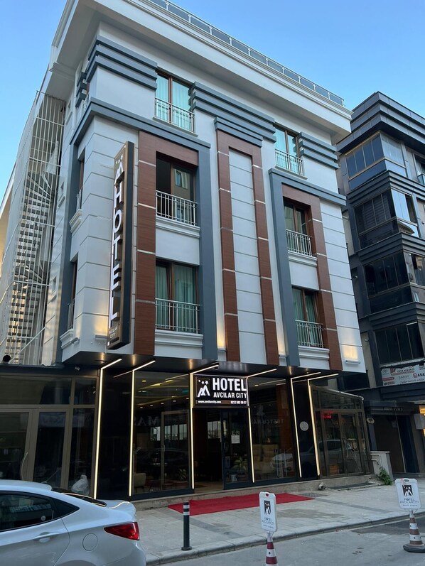 A modern hotel building with a prominent 'HOTEL' sign, large windows, and a red carpet entrance. - Hotel Avcilar City (Istanbul)