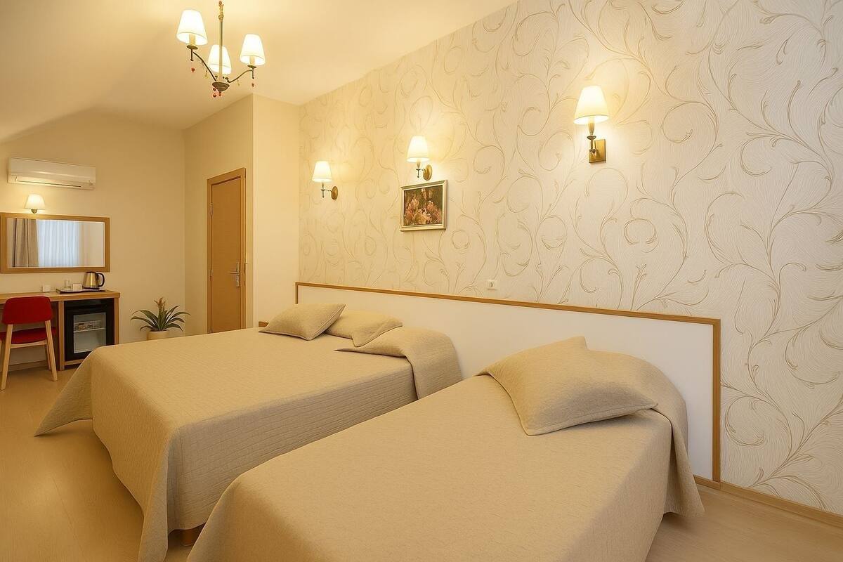 A hotel room with two beds, a desk, a chair, and a small plant.