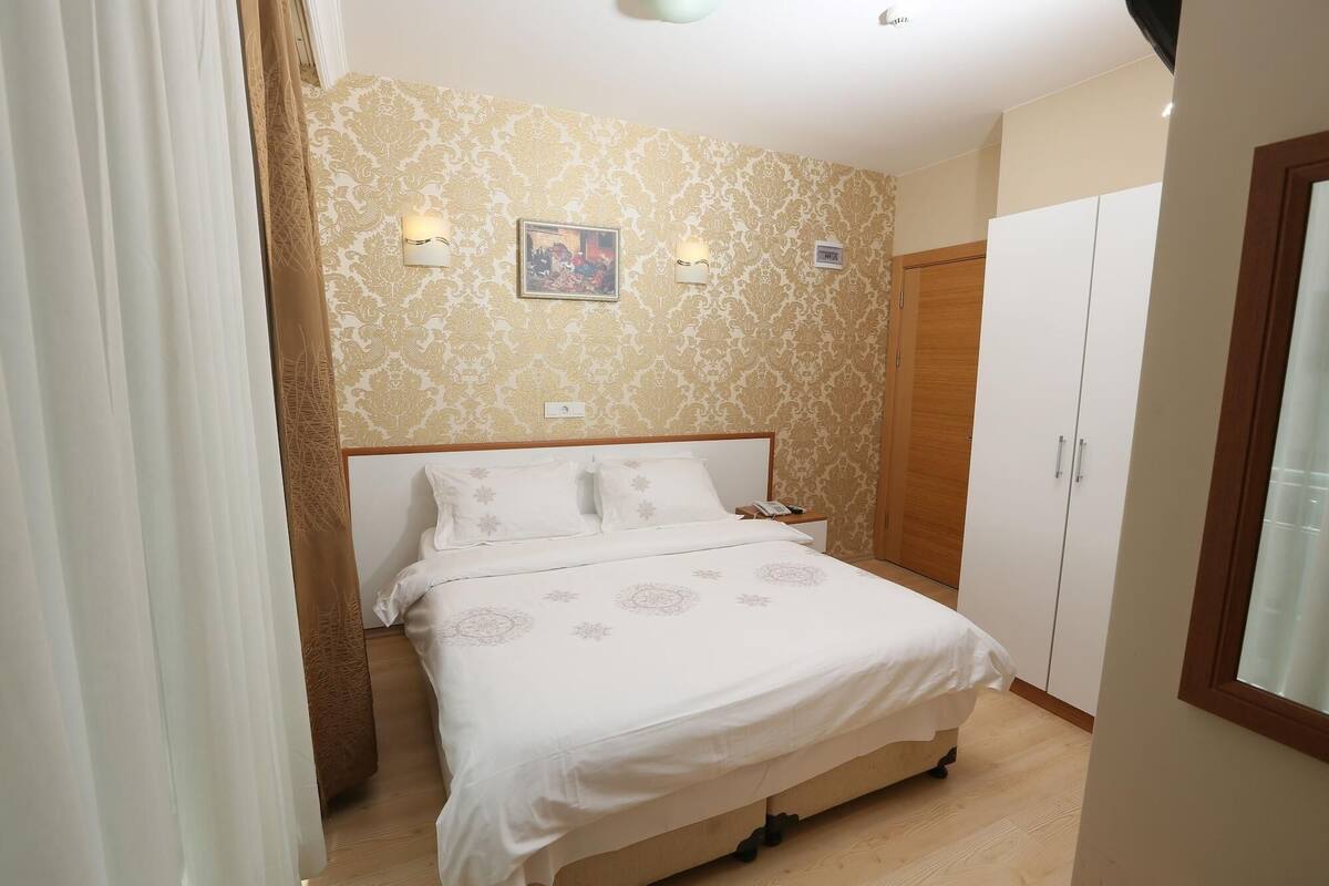 A bedroom with a bed, a nightstand, a wall clock, and a wardrobe.