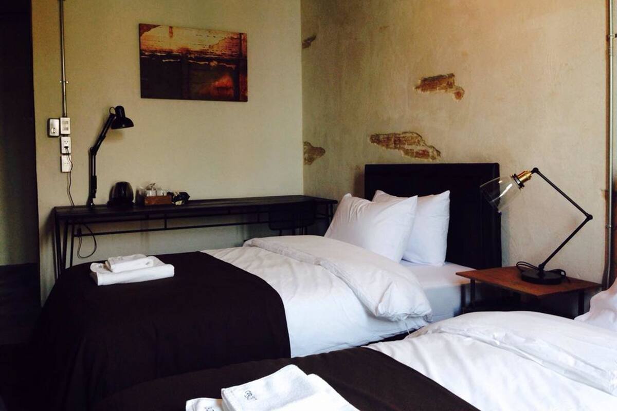 A hotel room with two beds, a desk, a lamp, and a painting on the wall.