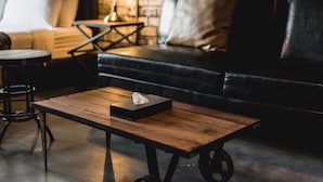 A cozy living area with a wooden coffee table, a black leather sofa, and a brick wall in the background. - Samantan Hotel at Nimman (Chiang Mai)
